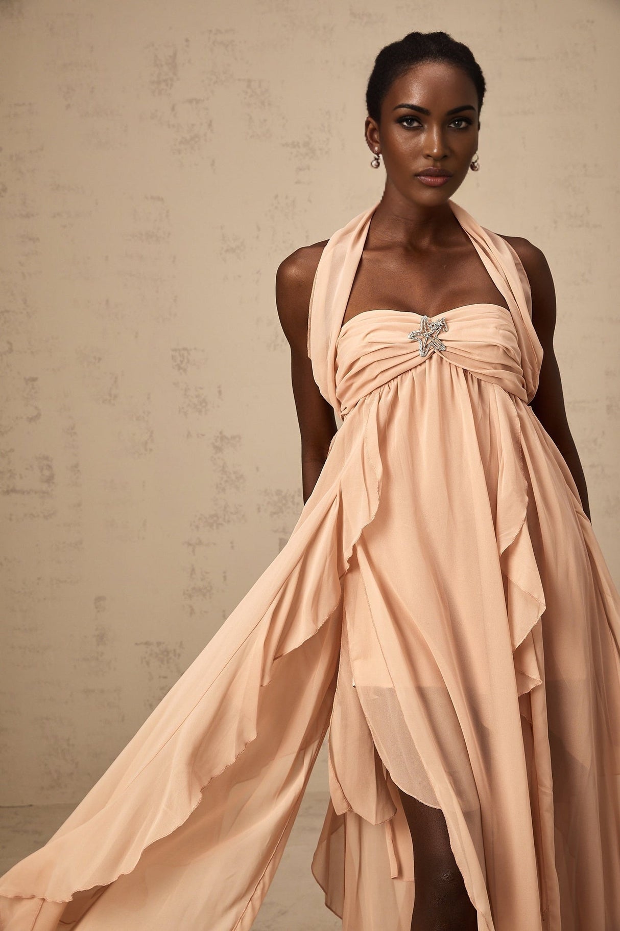 A long pink maxi dress with a halter neck and chiffon ruffles flowing down the body