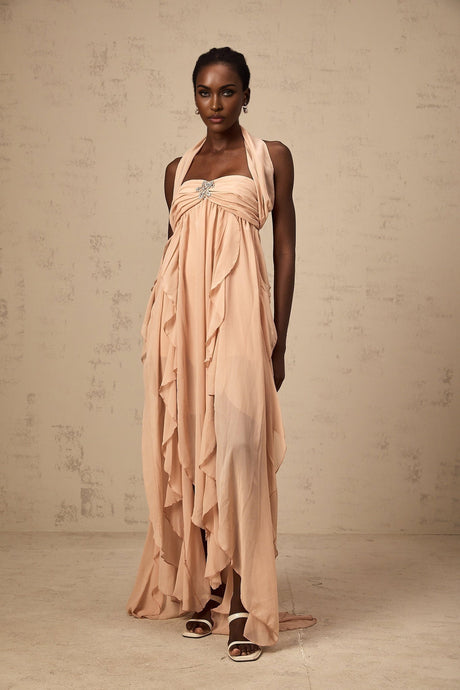 A long pink maxi dress with a halter neck and ruffled chiffon details worn by a model standing against a plain background