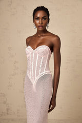 A long pink maxi dress with rhinestone embellishments and sheer elements worn by a model against a plain background