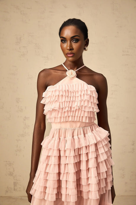 A long pink maxi dress with tiered ruffles and a tulle skirt featuring a petal shaped brooch at the waist