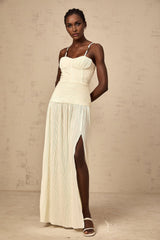 A long pleated maxi dress with side slits in neutral tones featuring a flowy silhouette and elegant design