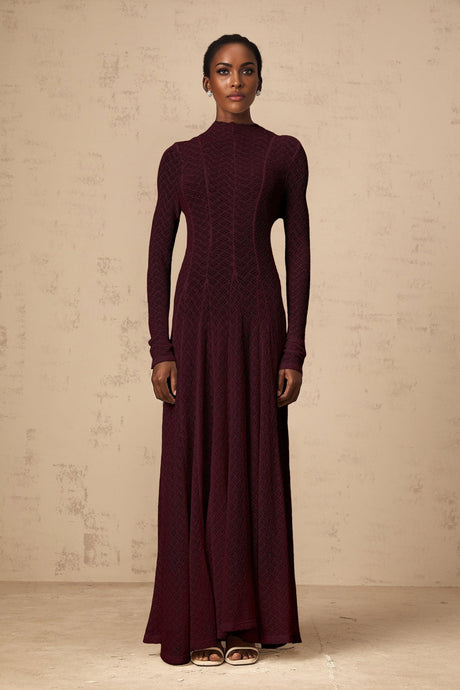 A long red lace maxi dress with a wavy pattern design worn by a model standing against a plain background