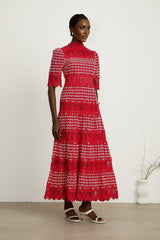 A long red maxi dress with scalloped lace panels featuring a floral pattern The dress has a fitted bodice and flowing skirt creating an elegant silhouette
