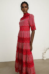 A long red maxi dress with scalloped lace panels featuring a floral pattern The dress has a fitted bodice and flows into a full length skirt