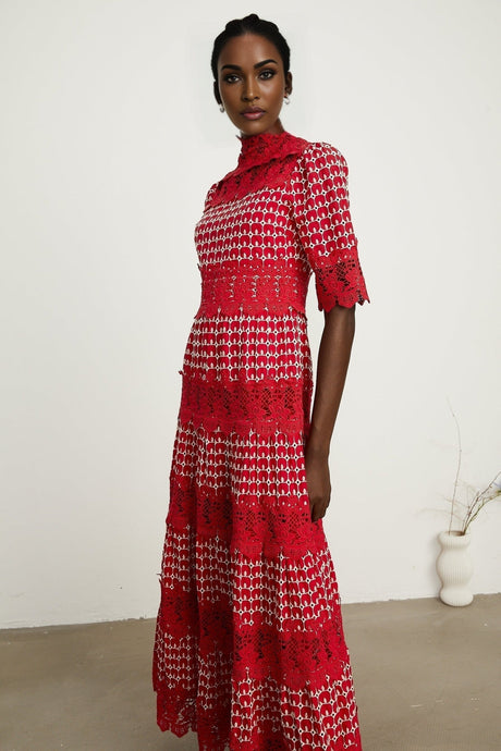 A long red maxi dress with scalloped lace panels featuring a floral pattern The dress has a fitted bodice and flows into a full length skirt