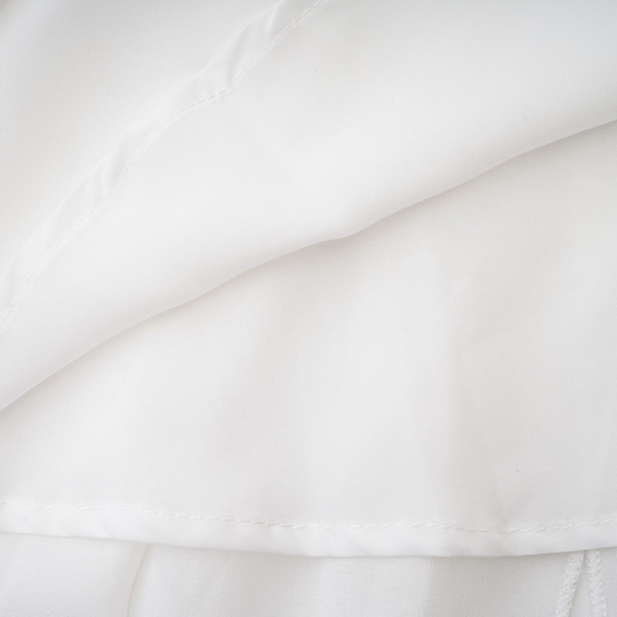 A long white chiffon maxi dress with a halter neck and ruffle details worn by a model against a plain background