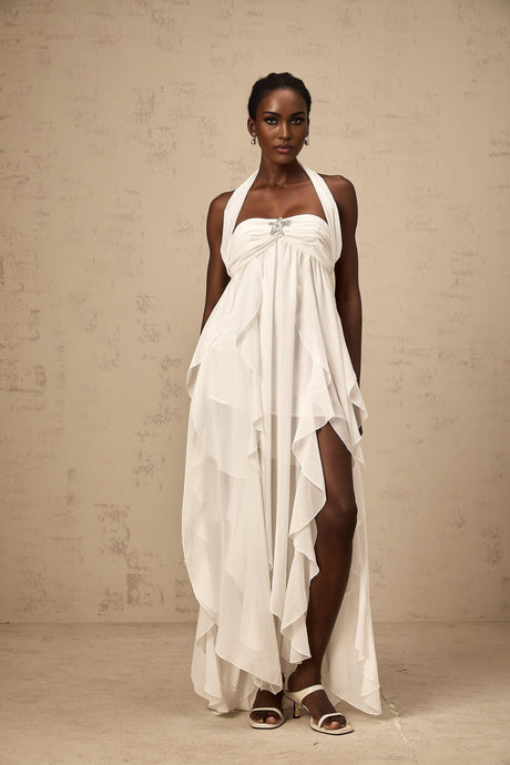 A long white chiffon maxi dress with a halter neck and ruffle details worn by a model standing against a plain background