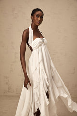 A long white chiffon maxi dress with ruffle details and a halter neckline worn by a model against a plain background