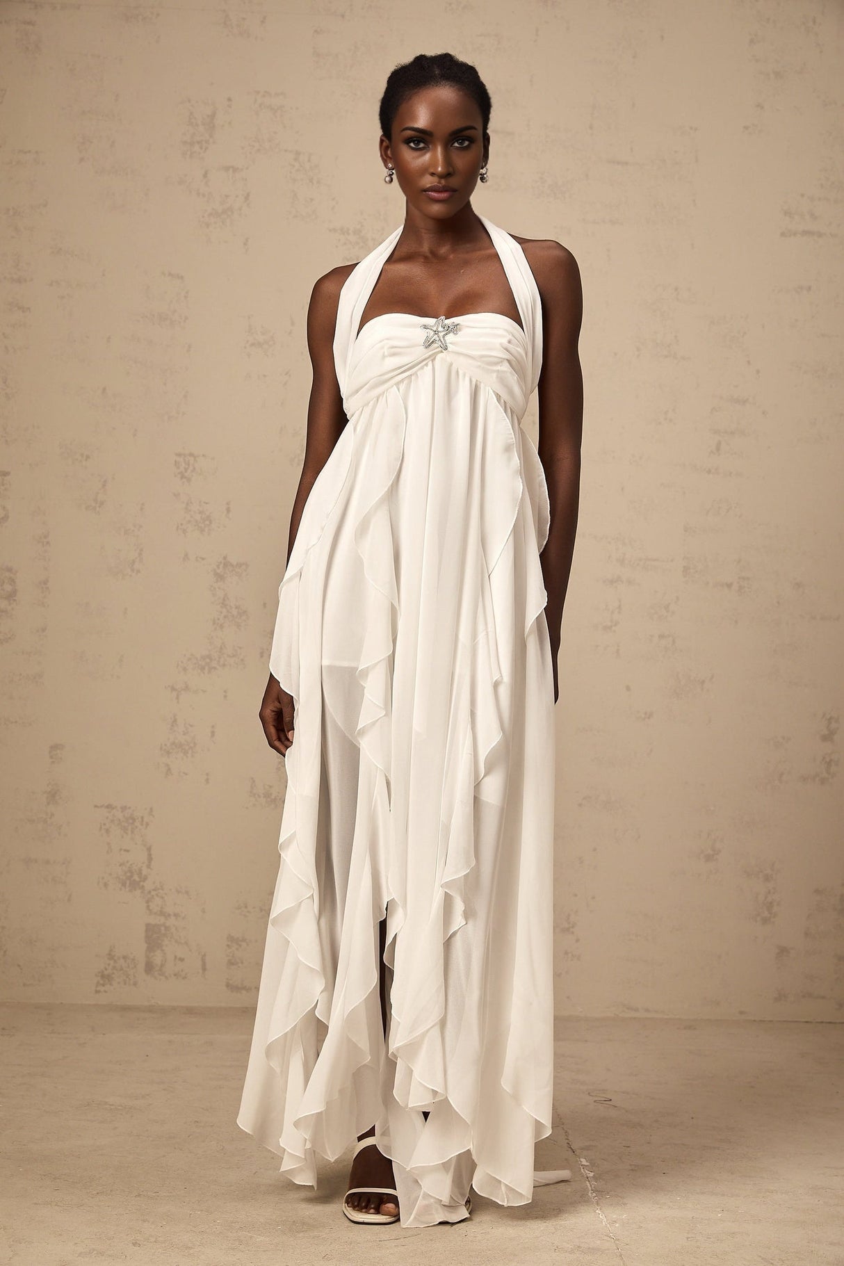 A long white chiffon maxi dress with ruffle details and a halter neckline
