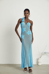 A long white crochet maxi dress with colorful faux flower embellishments adorning the bodice and straps