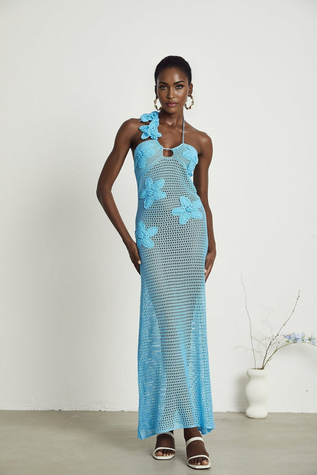 A long white crochet maxi dress with colorful faux flower embellishments adorning the bodice and straps