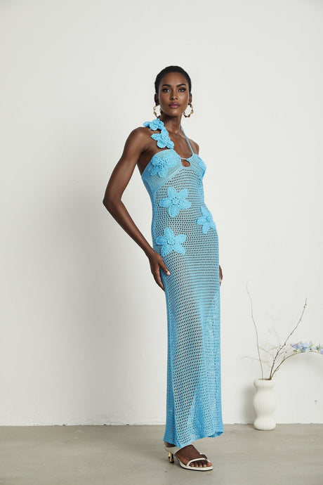 A long white crochet maxi dress with colorful faux flower embellishments scattered throughout the design featuring a sleeveless silhouette and flowy skirt
