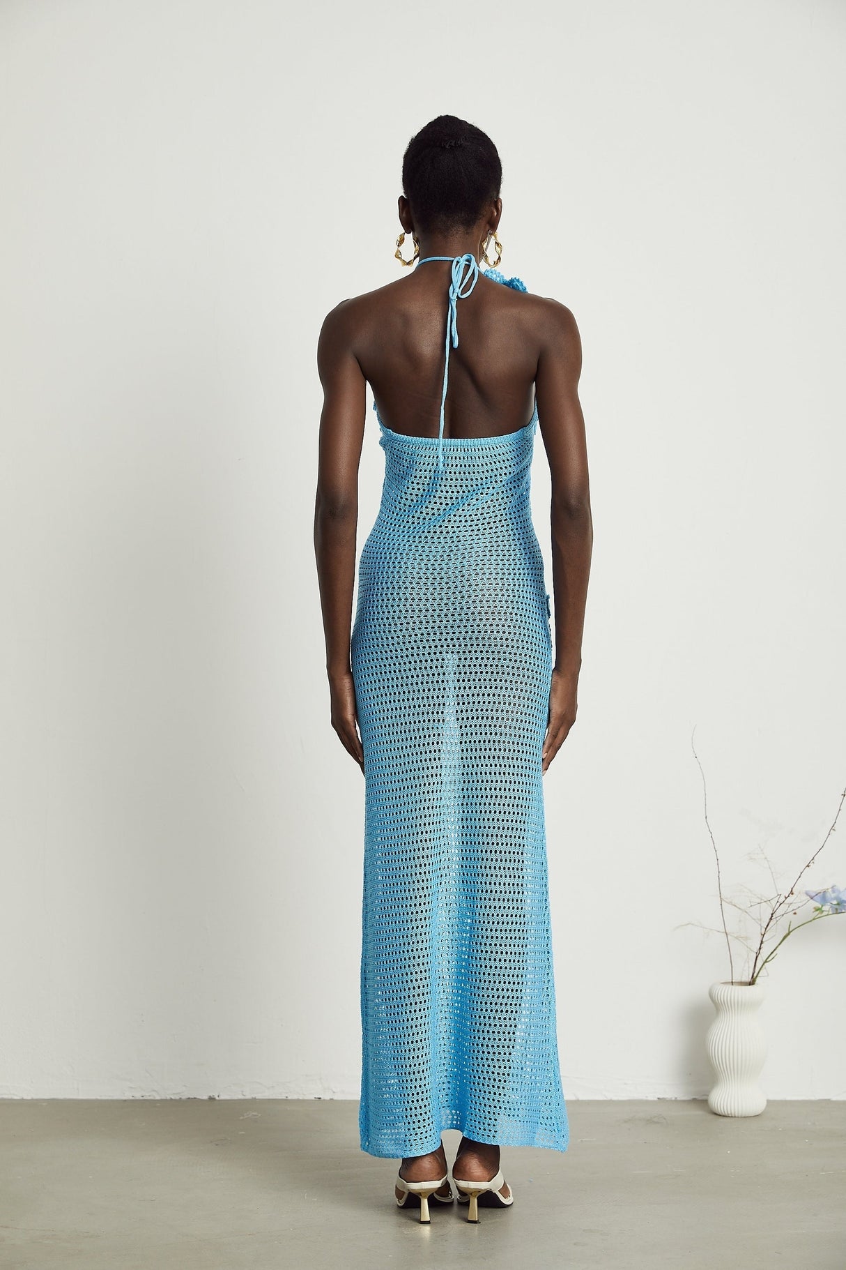 A long white crochet maxi dress with colorful faux flower embellishments scattered throughout the design