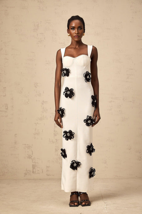 A long white formfitting maxi dress with floral applique details featuring a bandage style design worn by a model named Olivia