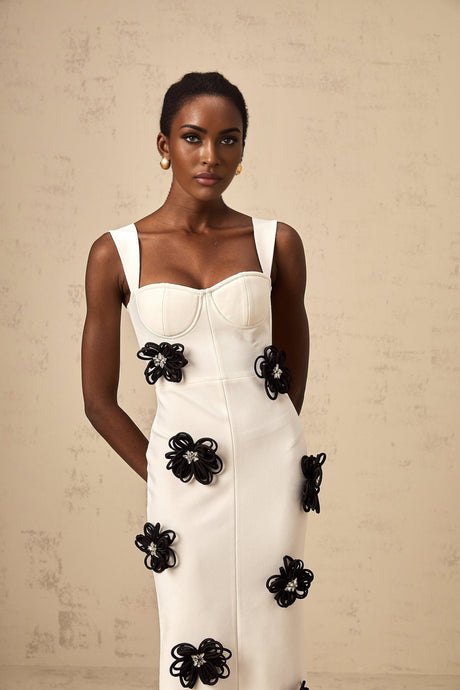 A long white formfitting maxi dress with floral appliqué details featuring a bandage style design worn by a model named Olivia