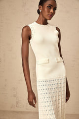 A long white knitted maxi dress with faux pearl embellishments adorning the garment