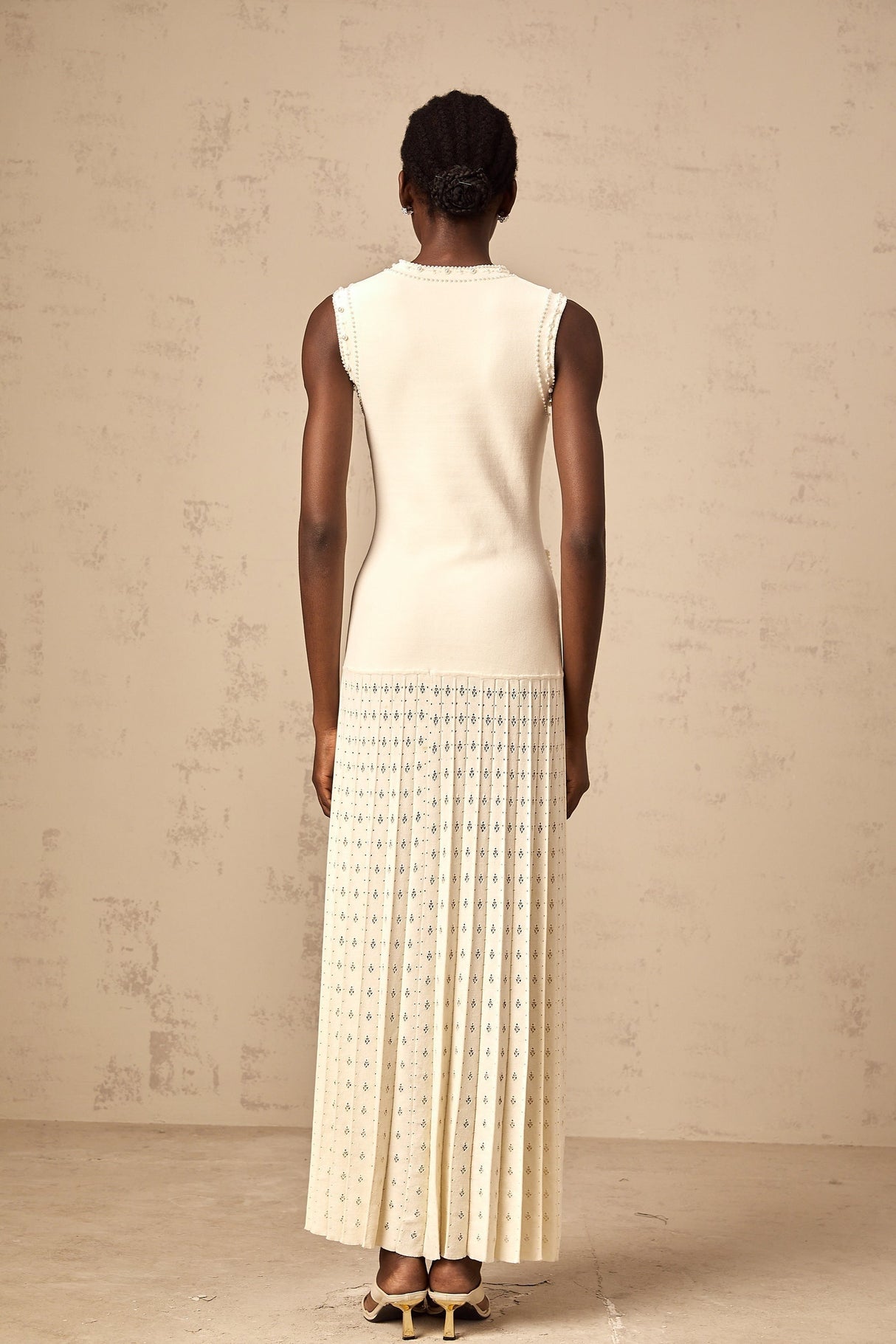 A long white knitted maxi dress with faux pearl embellishments throughout the fabric