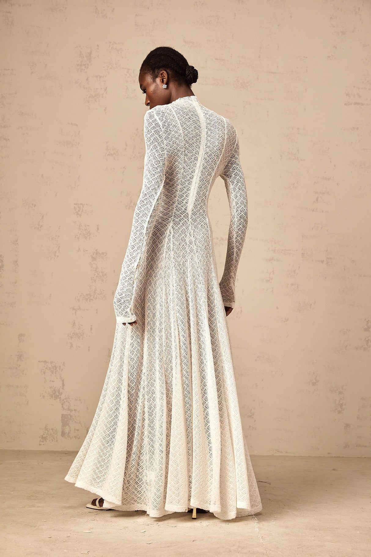 A long white lace maxi dress with a wavy pattern design worn by a model standing against a plain background