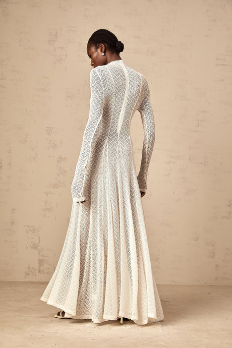 A long white lace maxi dress with a wavy pattern design worn by a model standing against a plain background