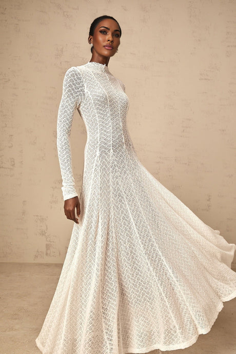 A long white lace maxi dress with a wavy pattern worn by a model standing against a plain background