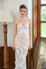 A long white maxi dress with a corset bodice featuring delicate floral applique details and a flowing skirt