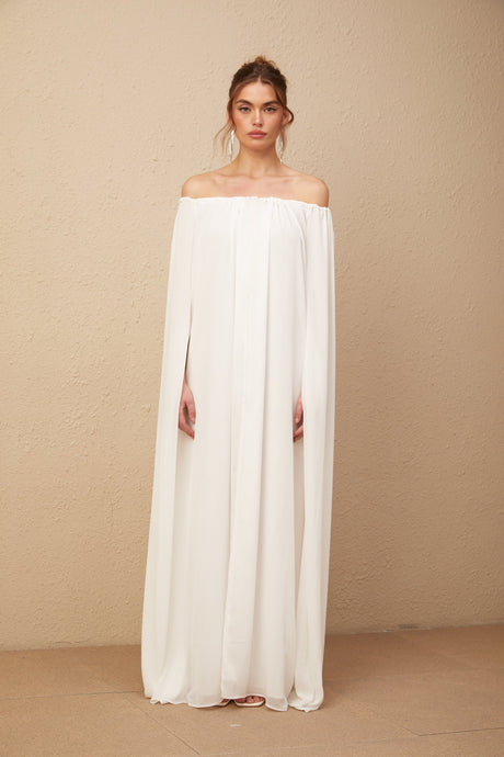 A long white maxi dress with a flowy tulle skirt and a capelike design draping over the shoulders creating an elegant and ethereal look