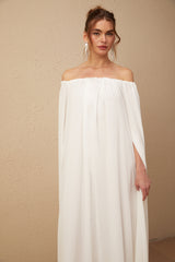 A long white maxi dress with a flowy tulle skirt and a capelike design draping over the shoulders creating an elegant silhouette