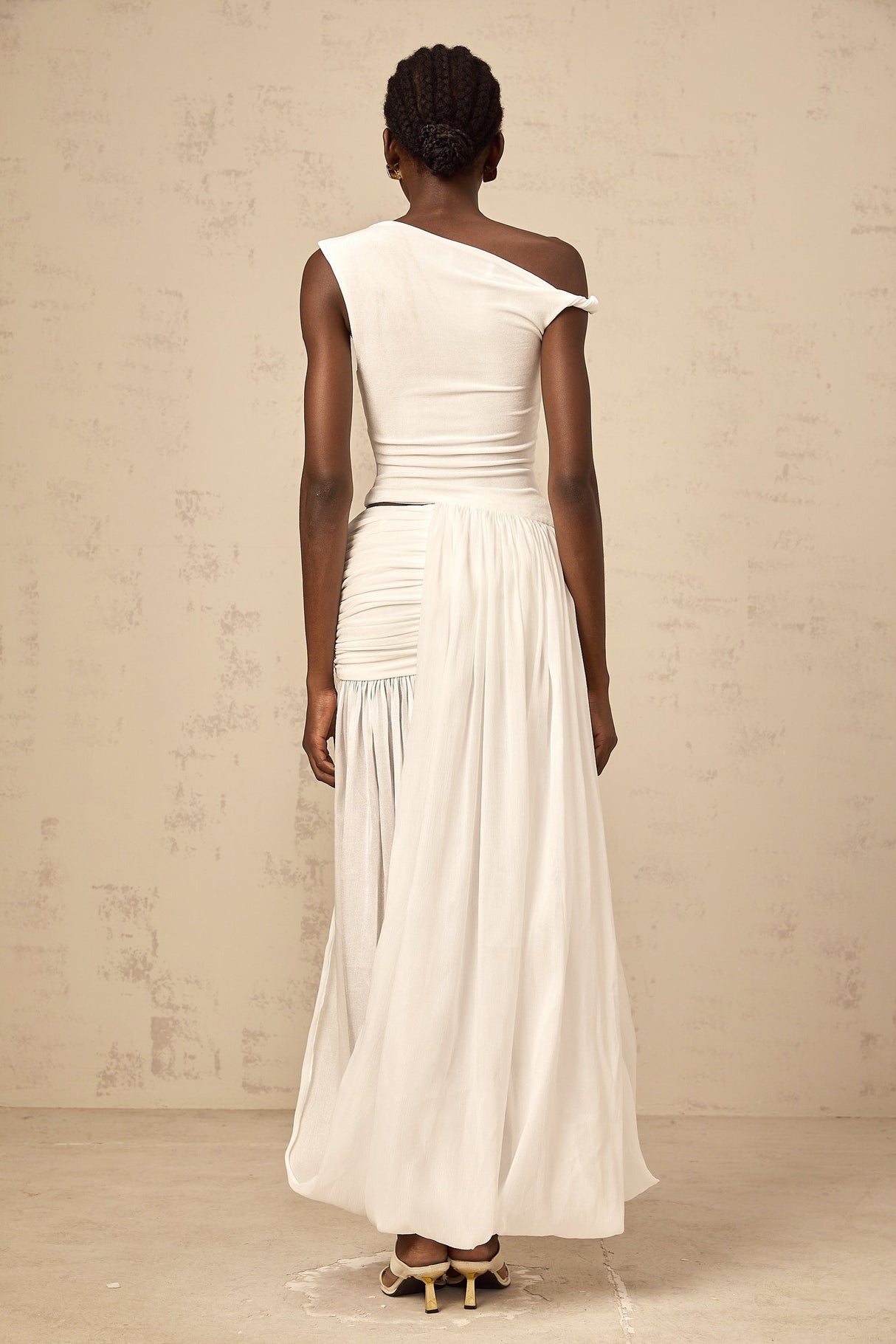 A long white maxi dress with a single shoulder strap and shirred panel detailing on the bodice