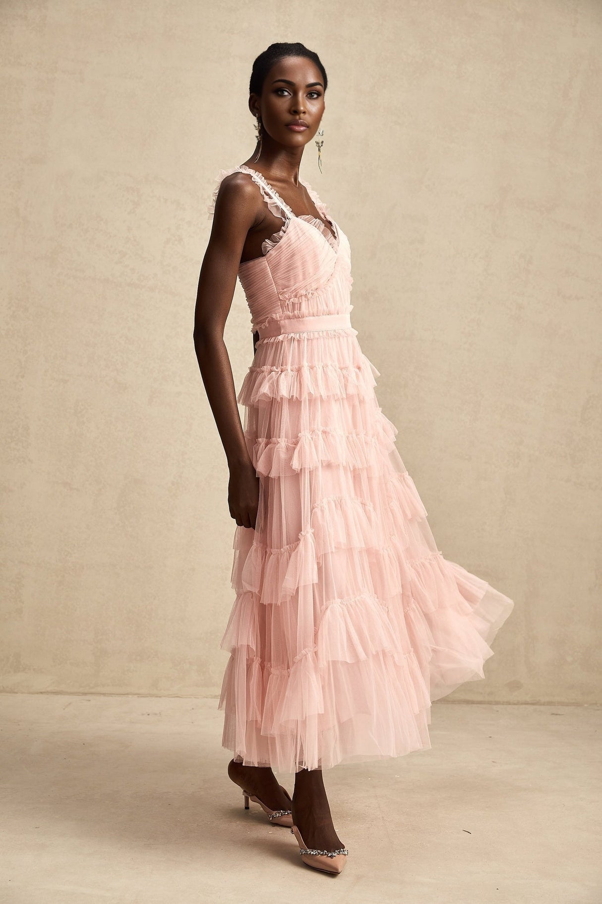 A long white maxi dress with layered ruffled tulle skirt and fitted bodice on a model against a plain background