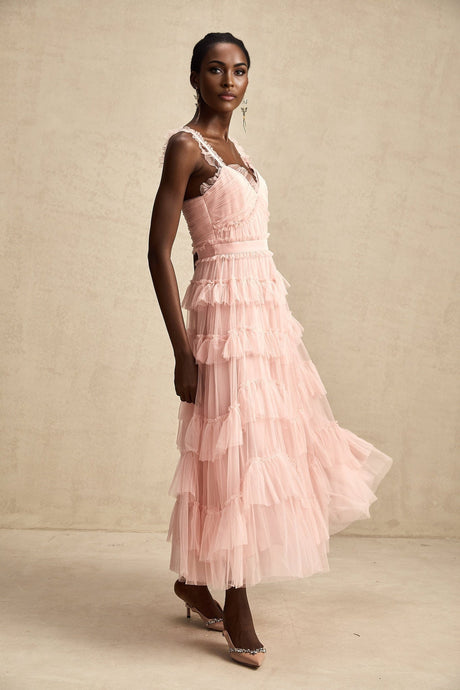 A long white maxi dress with layered ruffled tulle skirt and fitted bodice on a model against a plain background