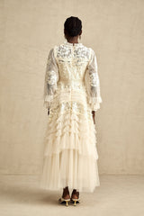 A long white maxi dress with sheer tulle layers and colorful floral embroidery details throughout featuring a flowing silhouette and delicate Capucine design