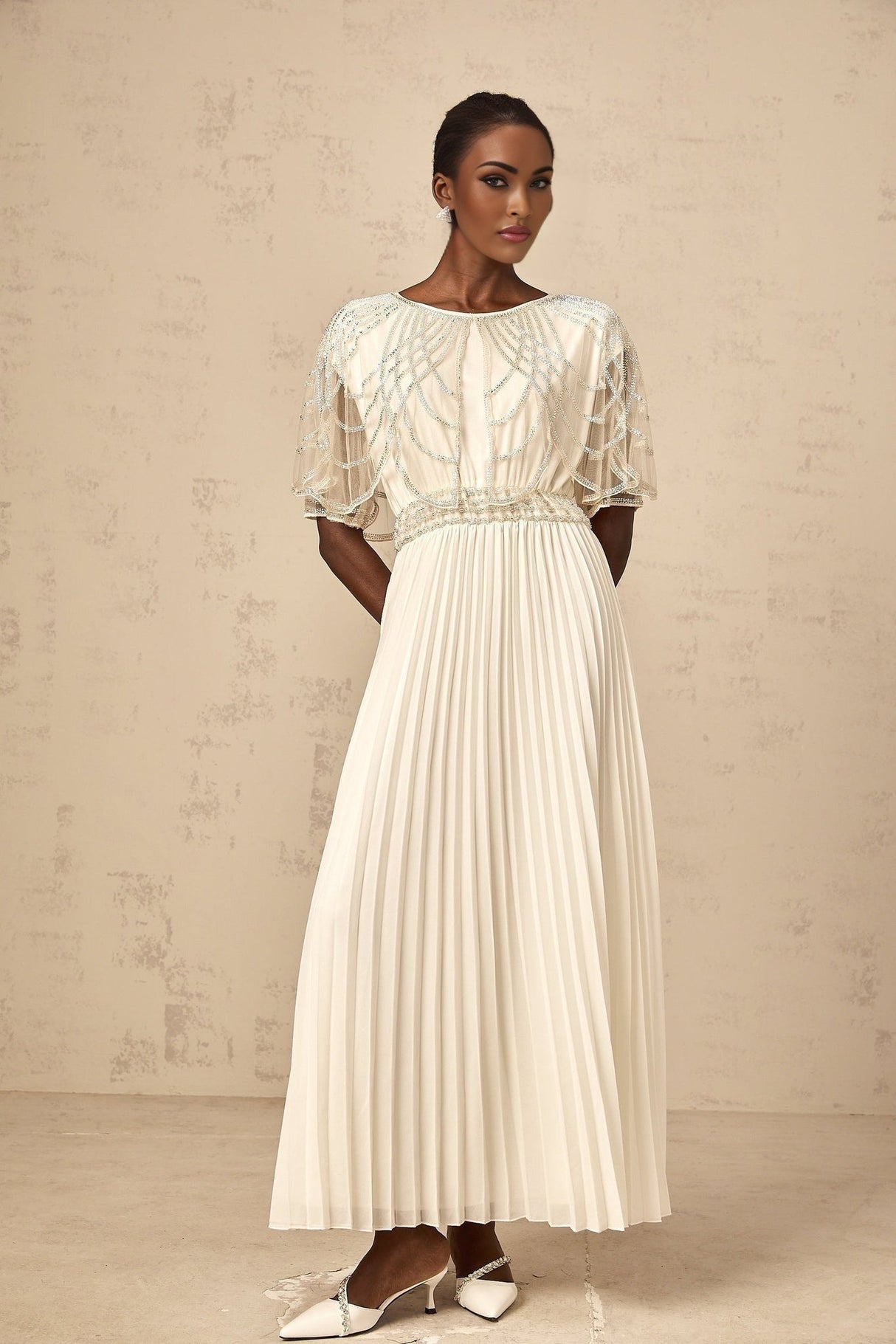 A long white pleated maxi dress adorned with crystal embellishments featuring a flowy silhouette and elegant design