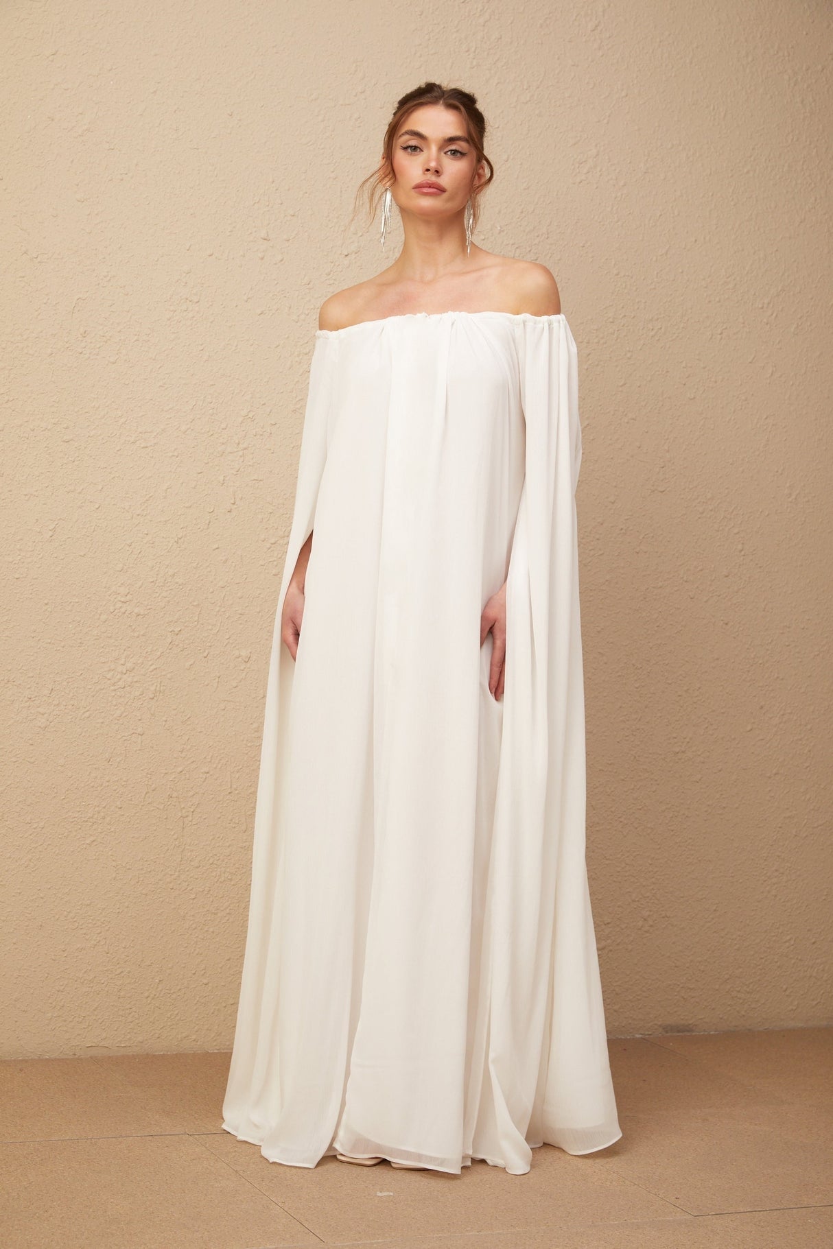 A long white tulle maxi dress with a capelike design and draped detailing named Patrizia