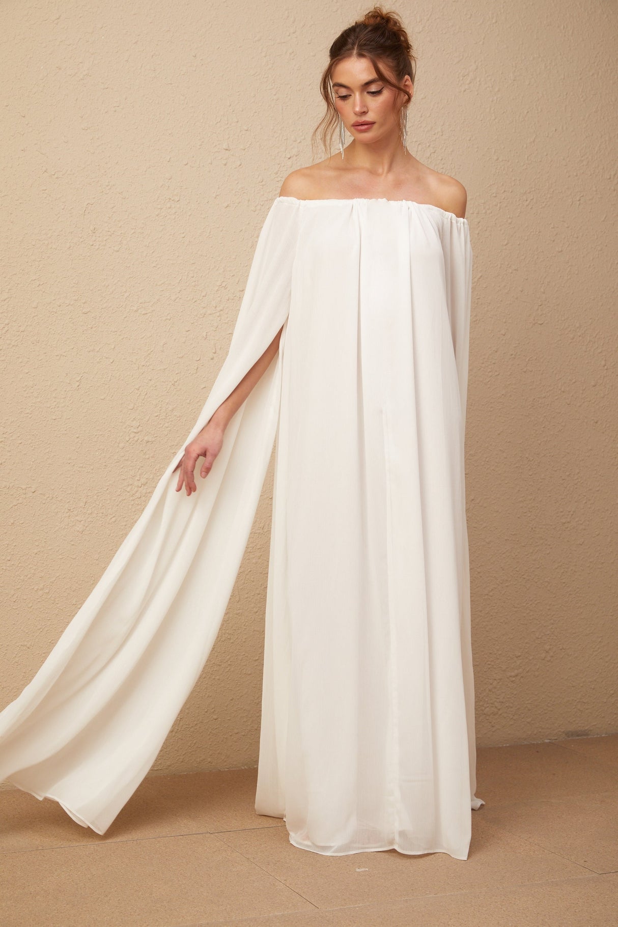 A long white tulle maxi dress with a flowing cape design and elegant draping