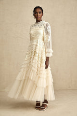 A long white tulle maxi dress with layers of sheer fabric featuring delicate floral embroidery in pastel colors
