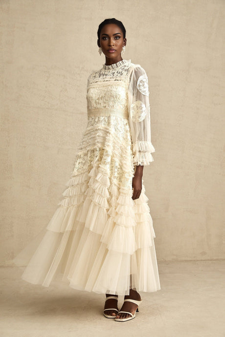 A long white tulle maxi dress with layers of sheer fabric featuring delicate floral embroidery in pastel colors