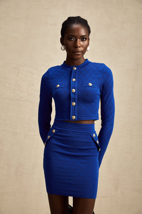 A matching set consisting of a blue knitted top and skirt The top features button details Both pieces are made by Maelys The outfit is designed to be worn together as a coordinated ensemble