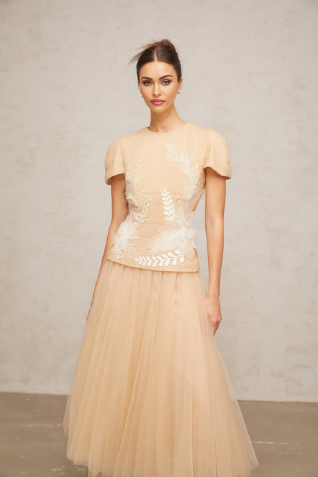 A matching set consisting of a top and skirt in white tulle fabric adorned with colorful floral appliqués The top features a sleeveless design while the skirt has a flowing silhouette Both pieces are decorated with delicate flower embellishments creating a romantic and feminine look