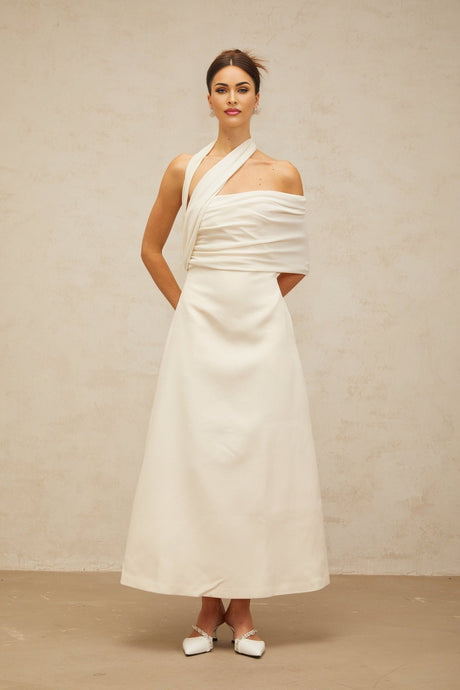 A model wearing a long creamwhite dress with an asymmetric design featuring a high slit and flowing fabric
