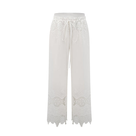 A model wearing a matching set consisting of a cropped top and trousers in white The top features lace trim and cutout details The trousers are high waisted and flared The set has a romantic and feminine style