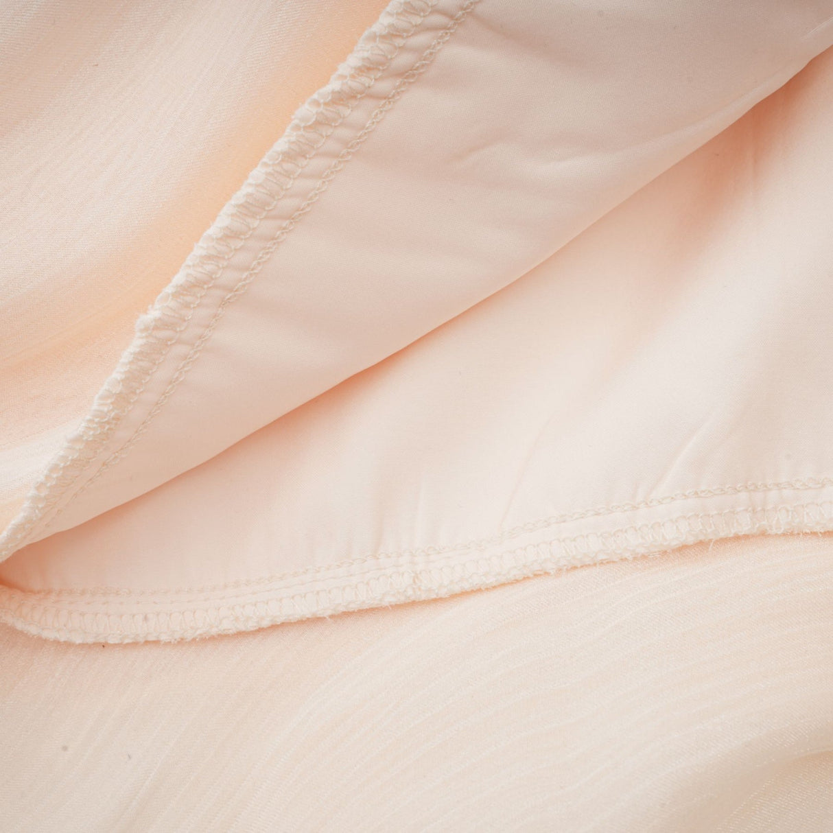 A neutral colored mini dress with full pleats and ruffles featuring a feminine Eugenie style design