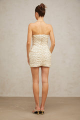 A neutralcolored mini dress with polka dot pattern and ruched detailing featuring a short hemline and fitted silhouette