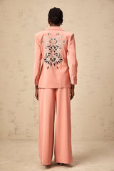 A pink blazer and trouser set with embroidery details and cutout designs The blazer features a tailored silhouette with decorative cutouts while the matching trousers have a sleek fit Both pieces are adorned with intricate pink embroidery creating an elegant and coordinated outfit