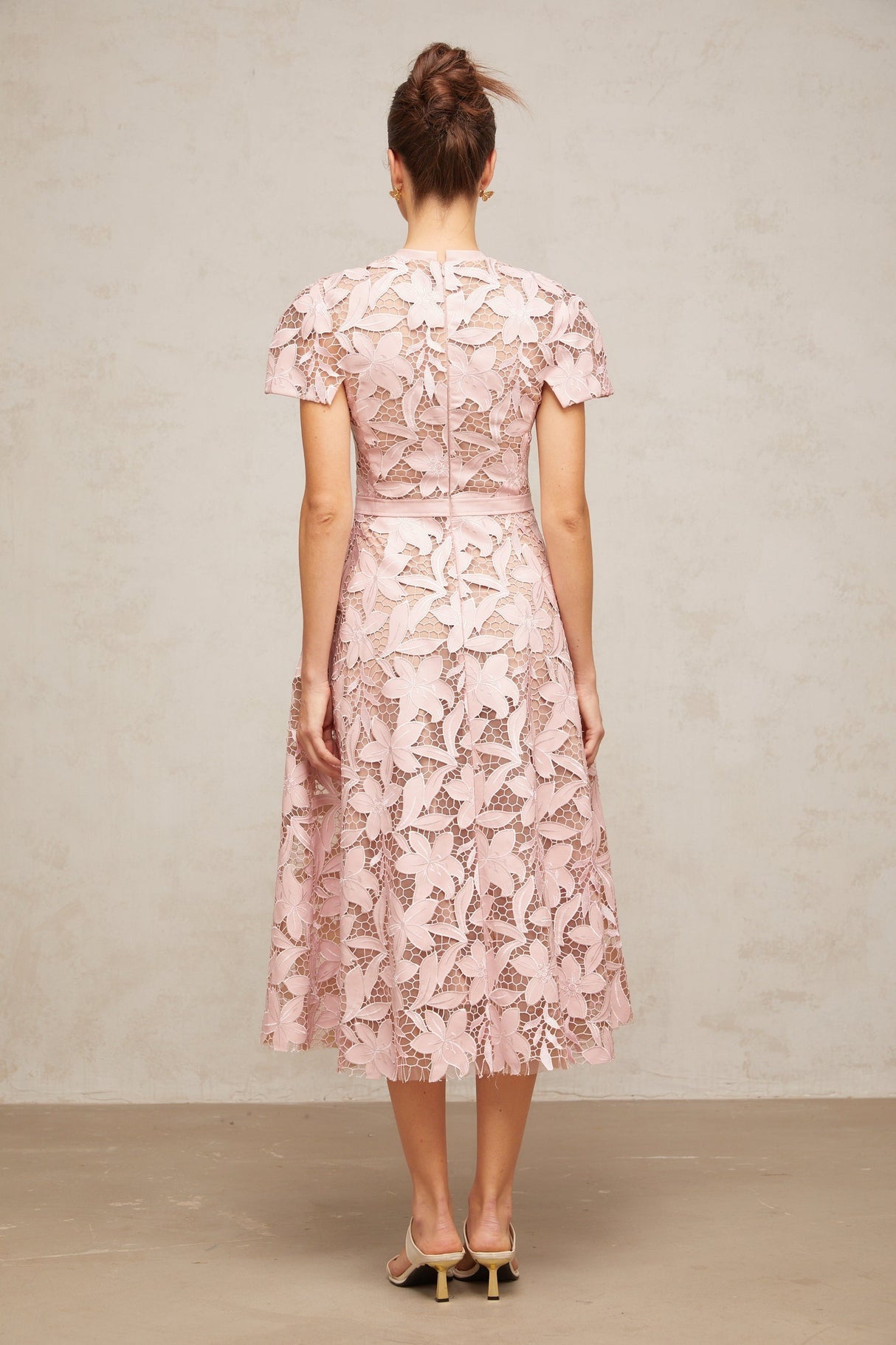 A pink midi dress made of delicate guipure lace featuring intricate floral patterns and a feminine silhouette