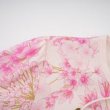 A pink midi dress with a floral print pattern worn by a model standing against a plain background