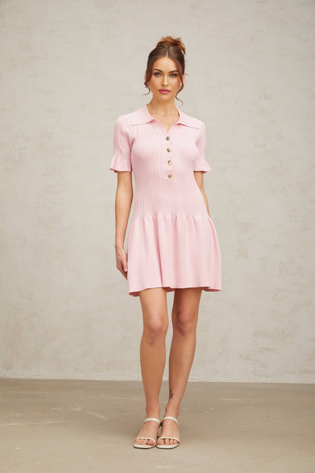 A pink mini dress with a flared skirt and fine knit texture worn by a model standing against a plain background