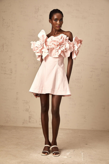 A pink mini dress with an offshoulder neckline adorned with three dimensional floral petal details