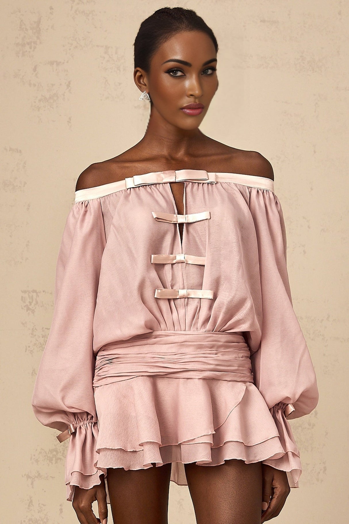 A pink offshoulder mini dress with a bow detail and flounced design worn by a model