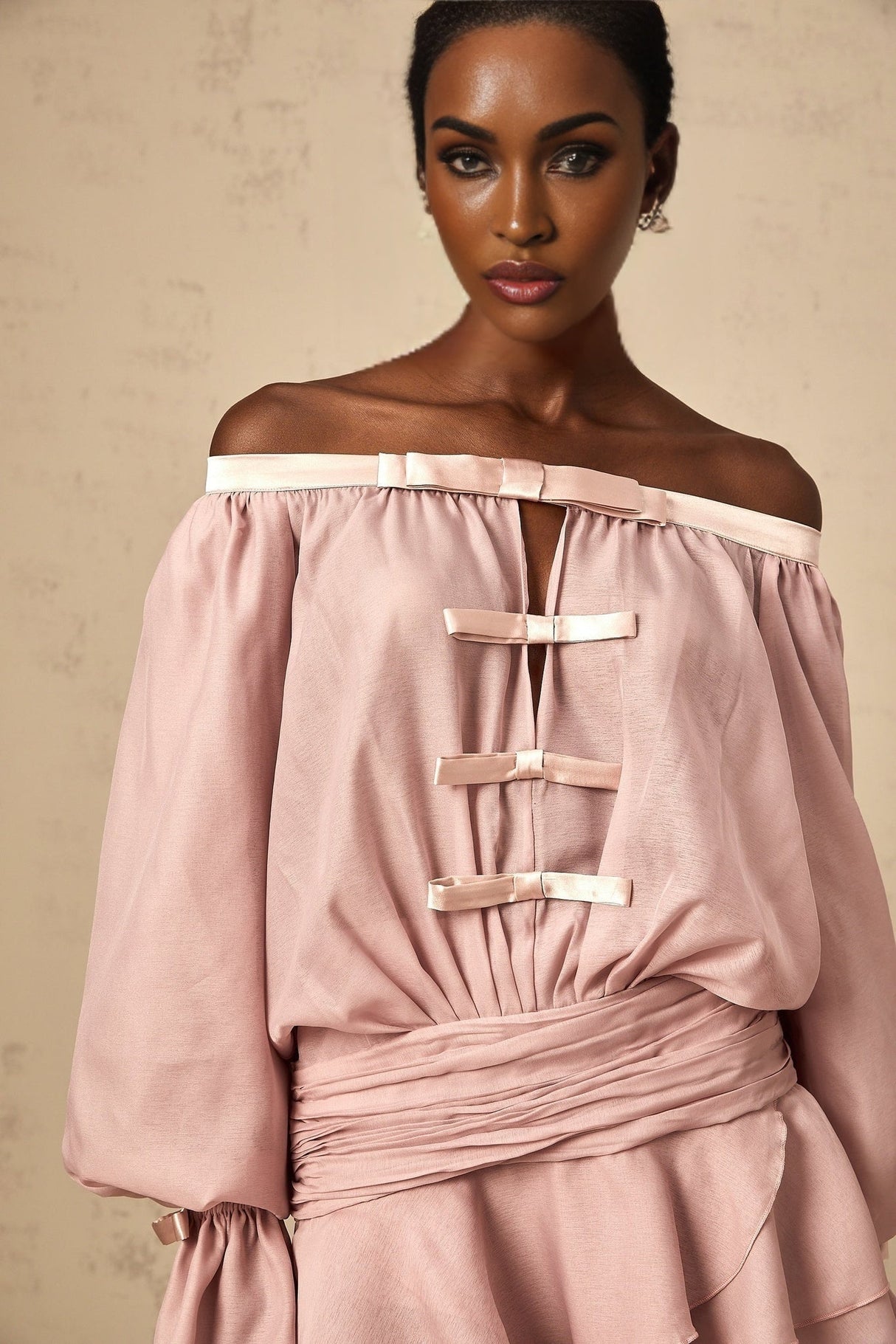 A pink offshoulder mini dress with a bow detail and ruffled hem