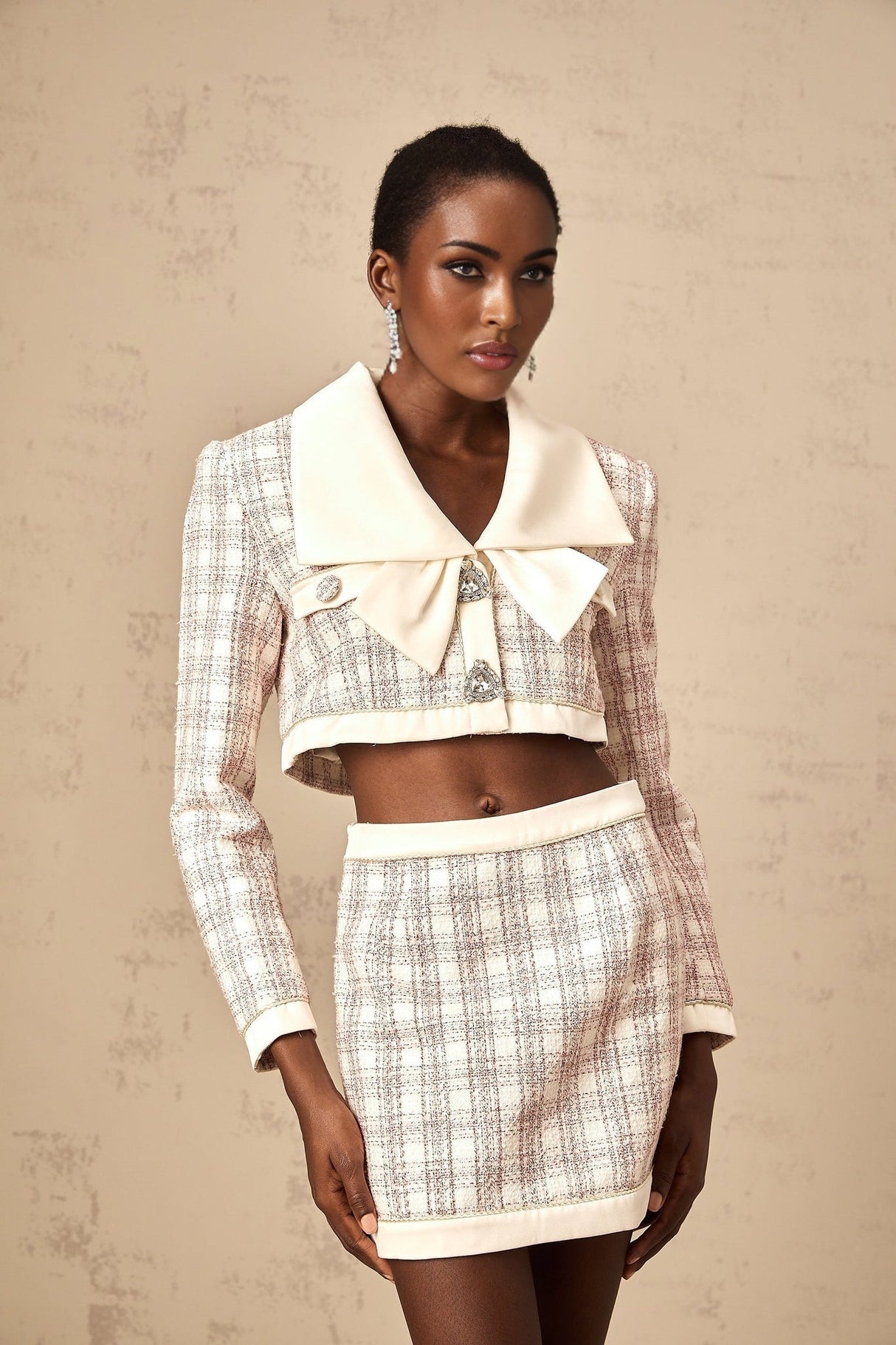 A pink tweed jacket and skirt set with a checked pattern The jacket has a tailored fit while the skirt is short and matching Both pieces feature the same pink tweed fabric with subtle checks throughout